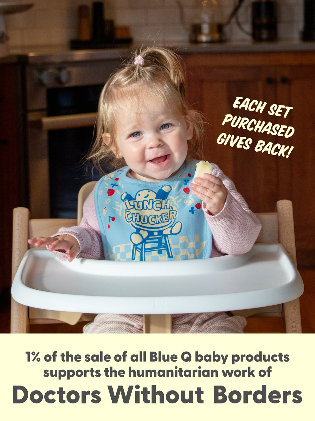A smiling toddler in a highchair wears a Blue Q “Sorry I’m Crabby. I Slept Like Garbage./Lunch Chucker” terry cotton bib and holds food. Each set purchased supports Doctors Without Borders.