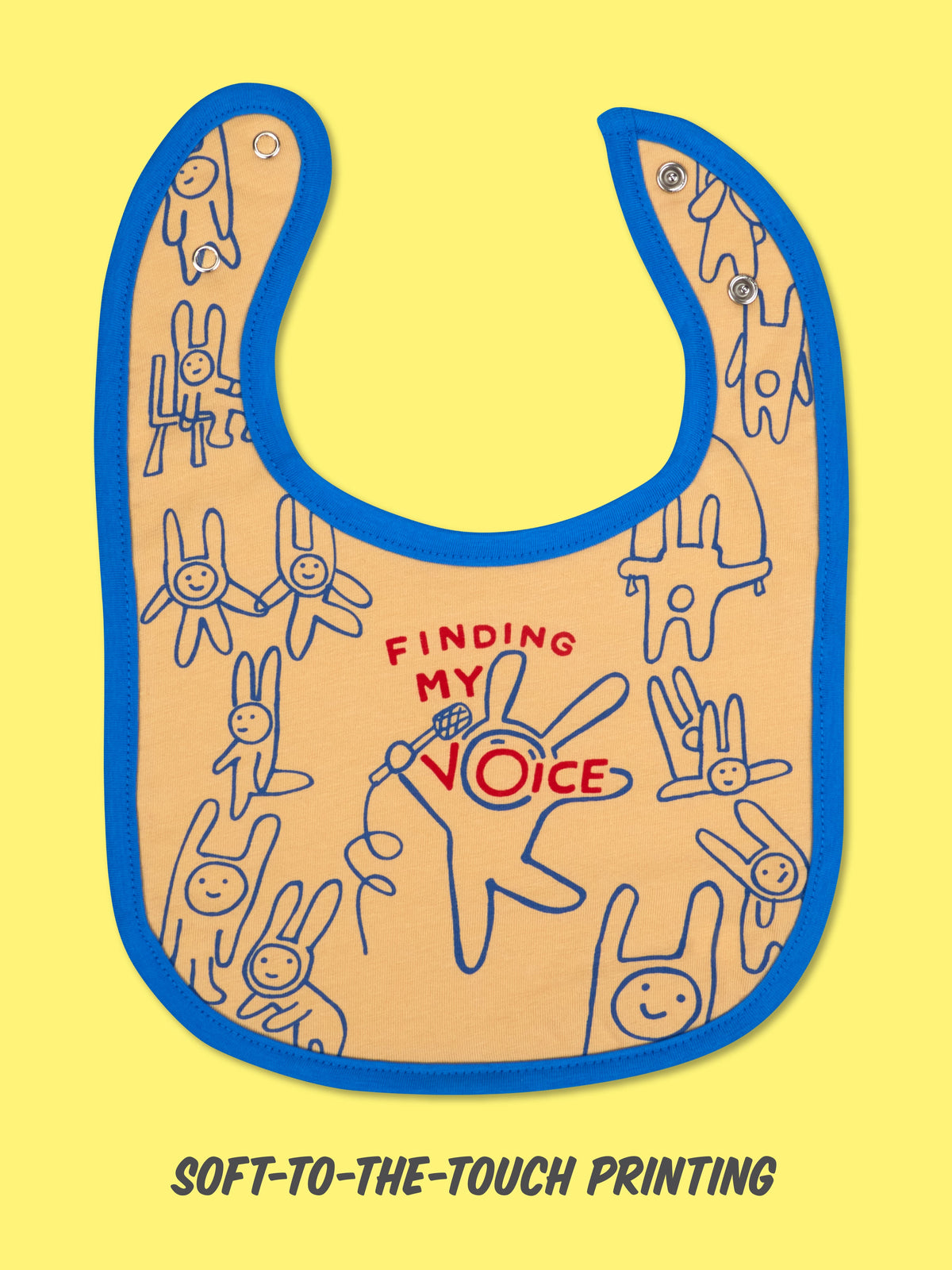 The Blue Q "Ten Moods In Ten Minutes/Finding My Voice" baby bib is yellow with blue trim, playful doodle bunnies, a red mic graphic, and "FINDING MY VOICE" text. Soft-to-the-touch printing adds comfort to this charming terry back bib.