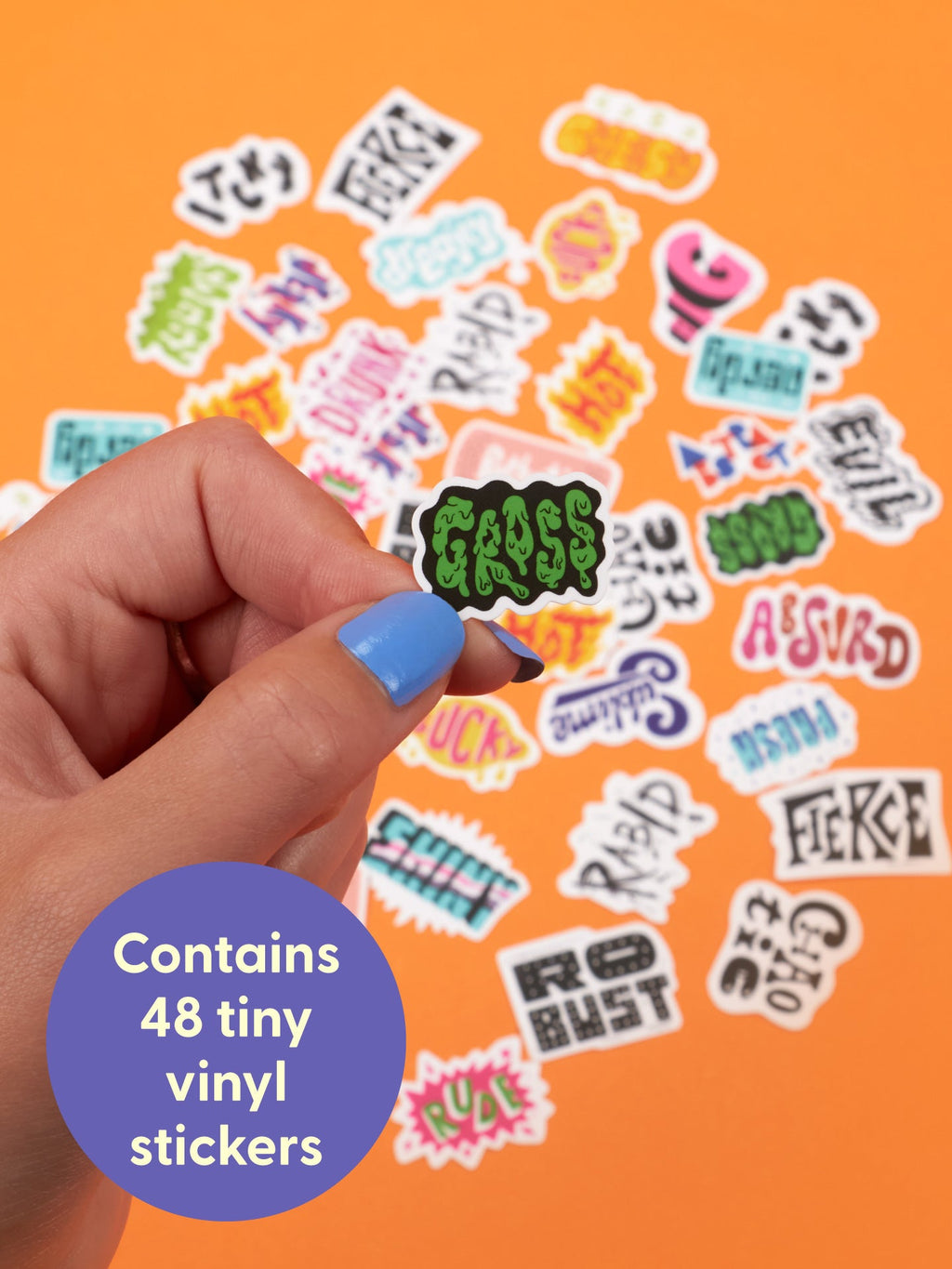 A hand holds an Amazing Adjectives Playtime Sticker Set sticker that reads GROSS over a collection of words that modify nouns scattered across an orange surface.
