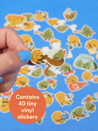 A hand holds up a Nugz Playtime Sticker Set, showing a small sticker of a cartoon nugget smoking a pipe next to a tree against a background of various cartoon stickers, with a label reading: Contains 40 tiny vinyl stickers.