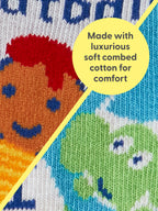 Close-up of Blue Q Little Meatball/I Get Heavy Baby Socks: colorful knitted fabric with smiling faces, divided diagonally. A yellow circle overlay reads, Made with luxurious soft combed cotton—fun and comfy!.