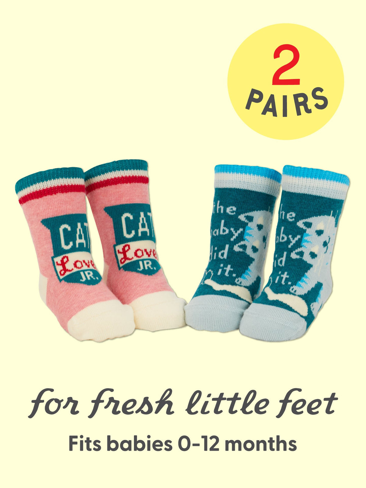 Two pairs of baby socks—one red and one blue—with playful cat designs and whimsical text from Blue Q’s Cat Lover Jr./The Baby Did It. Baby Socks collection. Made from soft organic cotton for comfort, plus a hint of spandex for just the right amount of stretch. Caption: for fresh little feet. Fits babies 0-12 months. A yellow circle notes: 2 pairs.