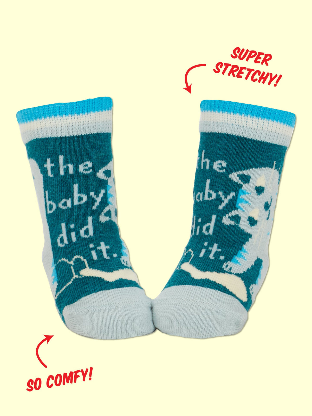 A pair of teal and white Blue Q Cat Lover Jr./ The Baby Did It. Baby Socks, crafted from soft organic cotton, featuring a playful cat design and the text “the baby did it.” Red annotations highlight SUPER STRETCHY! near the ankle—thanks to added spandex—and SO COMFY! near the toes.
