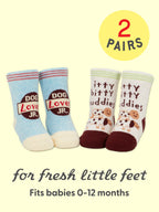 Keep your little one’s toes cozy with Blue Q’s Dog Lover Jr./Itty Bitty Buddies Baby Socks—two pairs designed for 0-12 months. Featuring one blue and cream pair with “Dog Lover JR.”, and another in cream and burgundy with playful dogs and itty bitty buddies, each set is crafted from soft organic cotton for all-day comfort. Text reads: 2 pairs for fresh little feet.