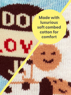 Close-up of colorful knitted fabric with playful patterns, divided by a yellow line. A yellow circle overlay reads, Made with luxurious soft combed cotton for comfort—Dog Lover Jr./Itty Bitty Buddies Baby Socks by Blue Q are the perfect organic cotton socks for you and your besties.
