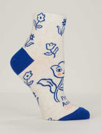The Pretty Anxious W-Ankle Socks by Blue Q are cream-colored women’s socks in combed cotton, with blue toe and heel, blue floral line art, and a cartoon fox with a flower. Fits shoe size 5-10; partial small text near the toe.