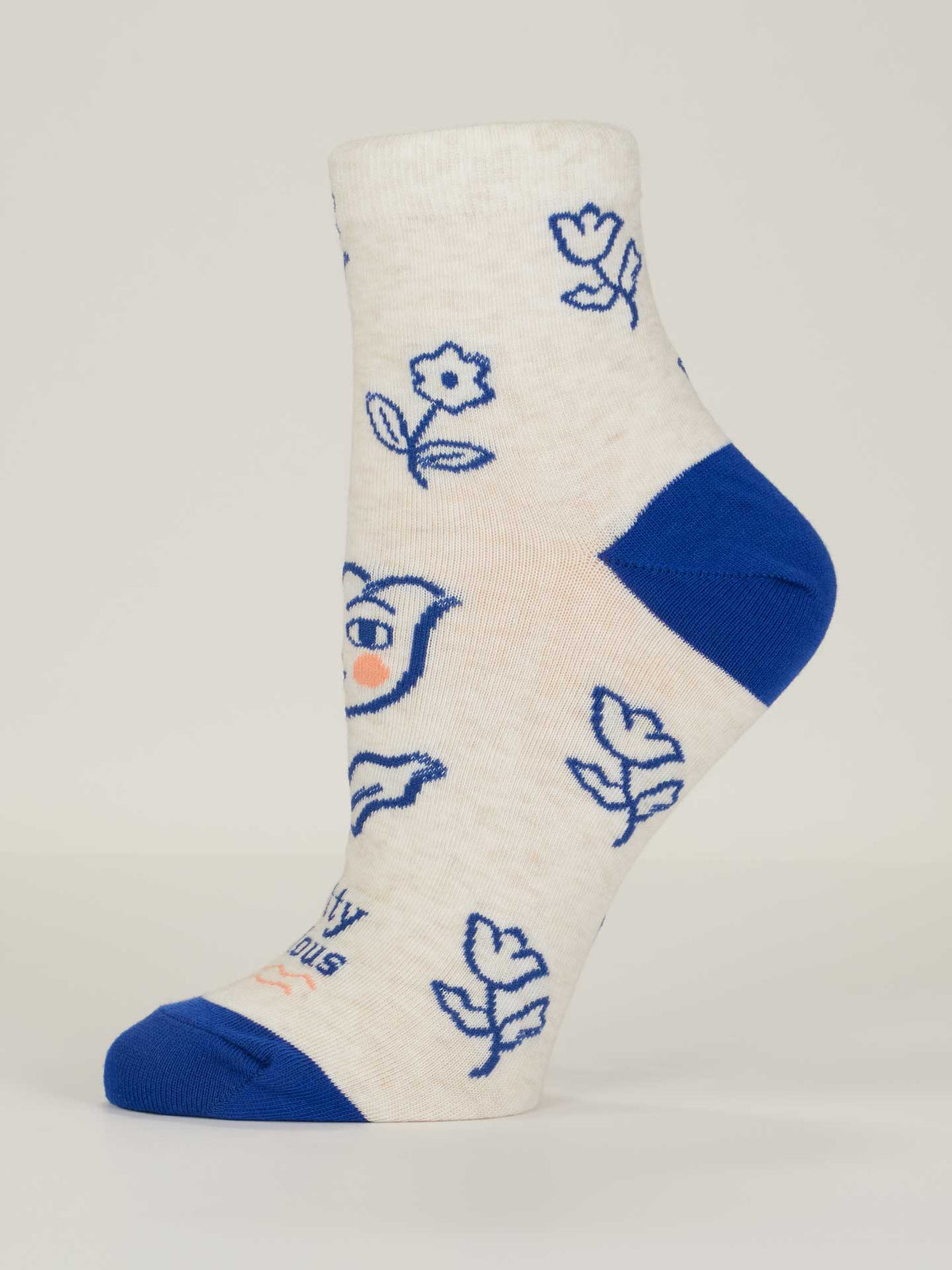 The Pretty Anxious W-Ankle Socks by Blue Q are white women’s socks (shoe size 5-10) with blue and pink cartoon flowers, a smiling face, blue toe and heel, shown on a mannequin foot against a plain background. Made from soft combed cotton.